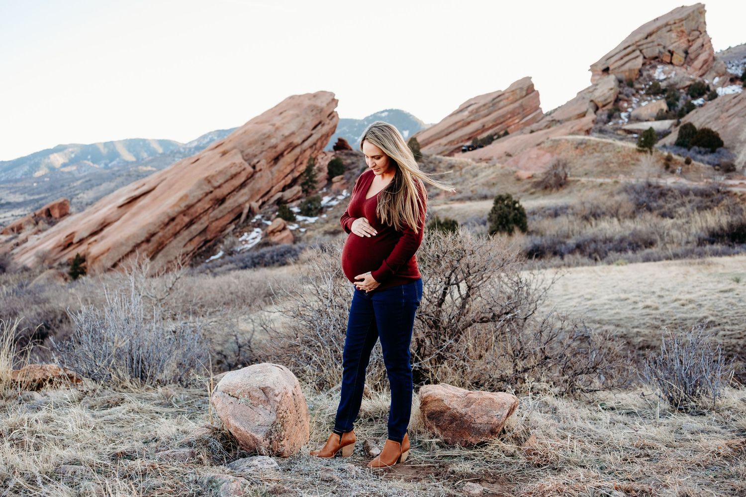 Pregnant mother standing, holding her belly, hair gently blowing in wind, stunning red rock formations in background.