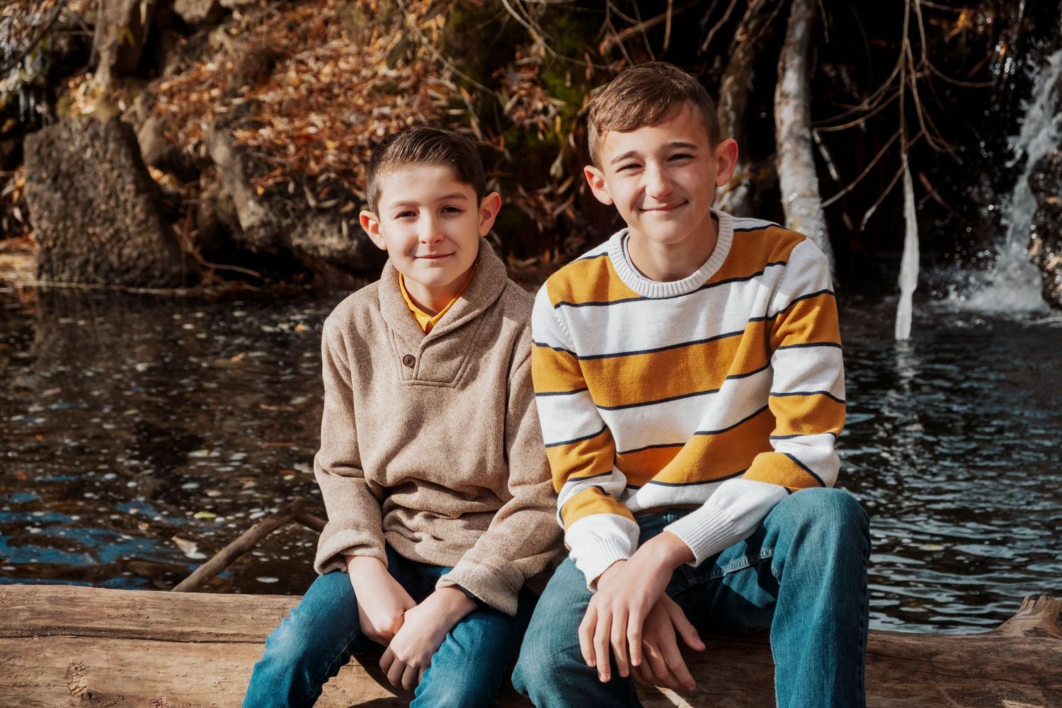 Two brothers sitting in front of waterfall at Golden Ponds Park in Longmont, Colorado.