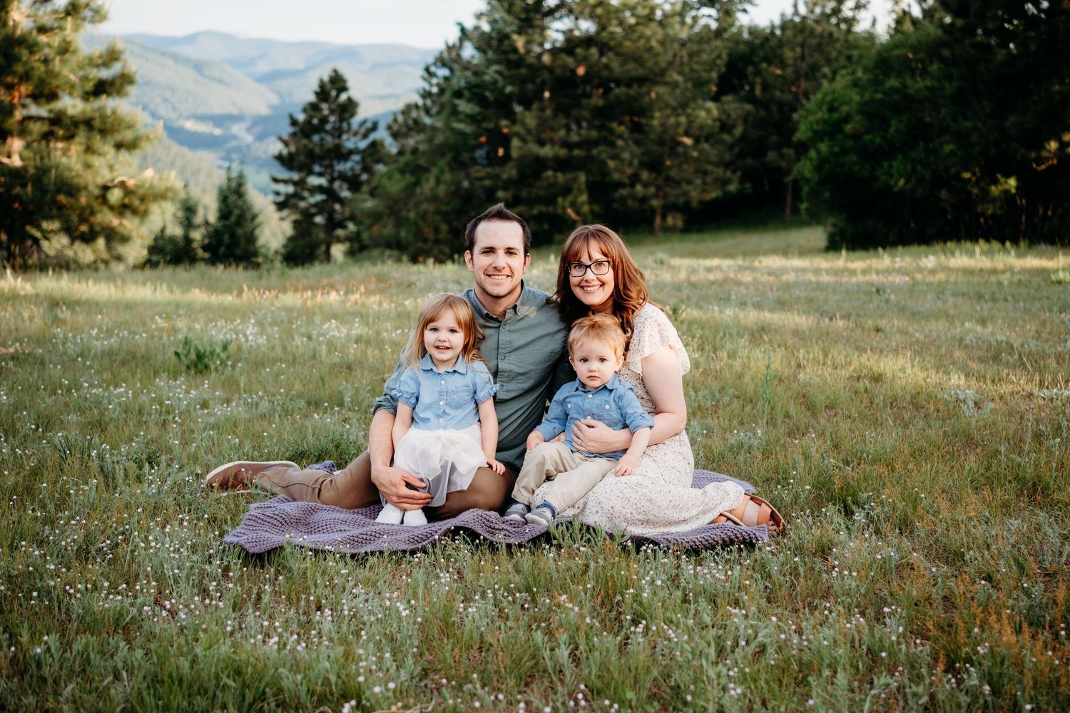 Father, mother, young daughter and toddler son sitting on blanket, all smiling, at Mt Falcon West family photo session.