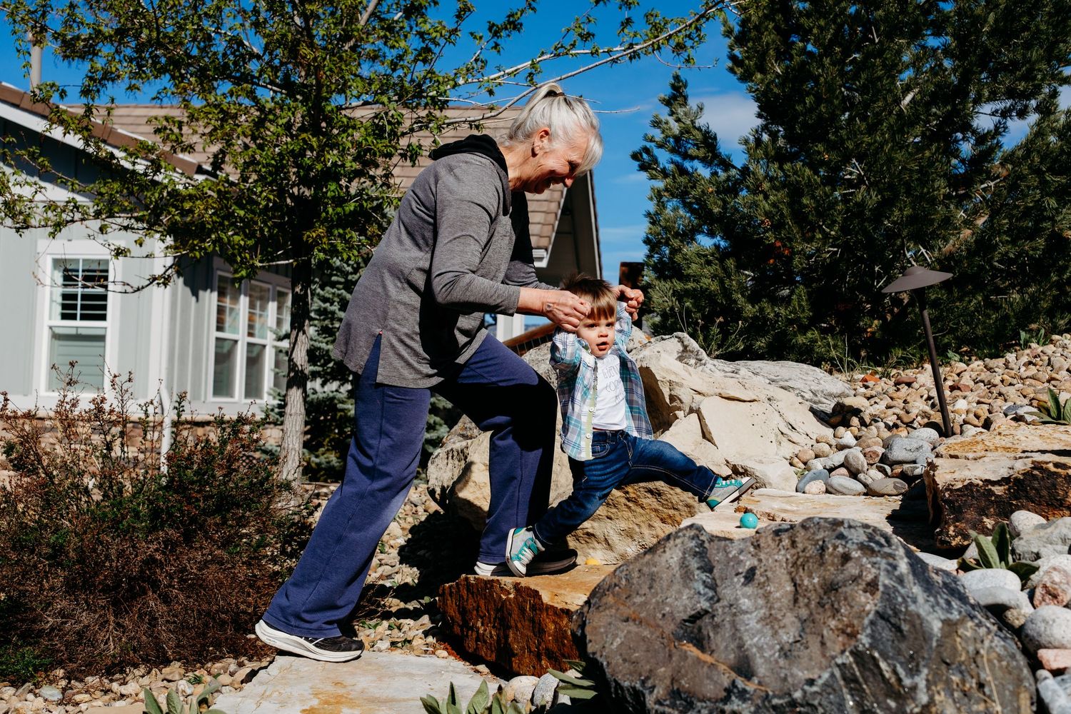 Grandmother helping grandson step up rocky steps in backyard.
