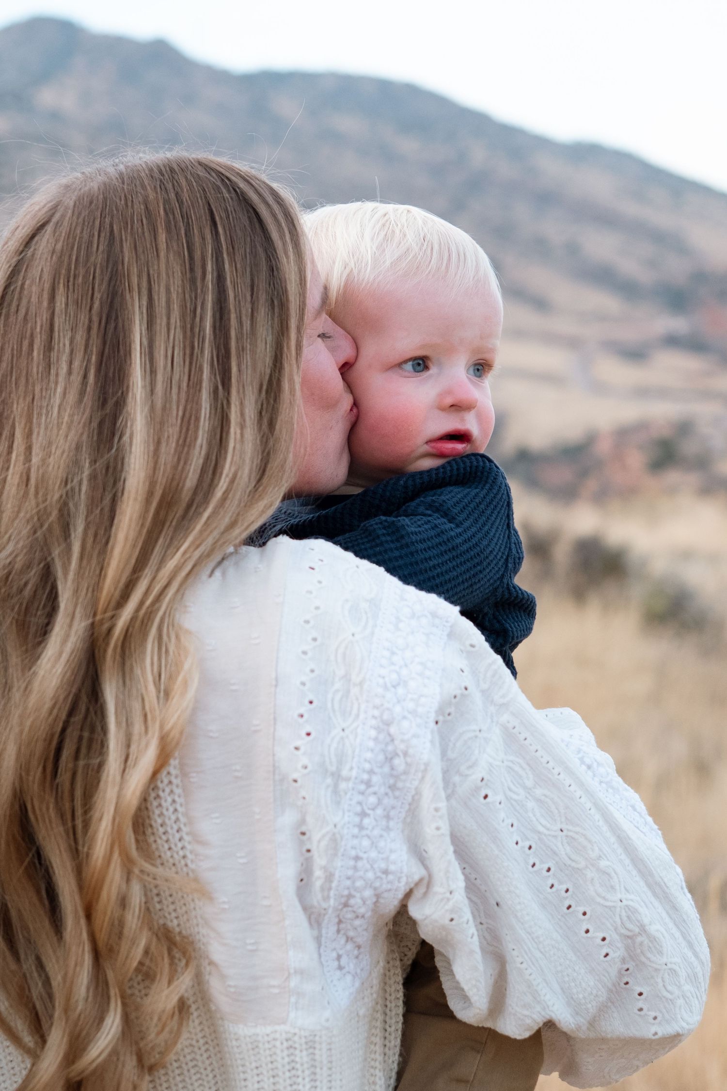 Mother kissing son's cheek, mothers long blond hair rolling down her shoulders.