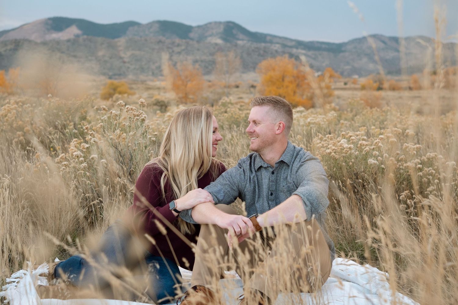 Adult couple smiling at one another at Bear Creek Lake Park with foothills in background.