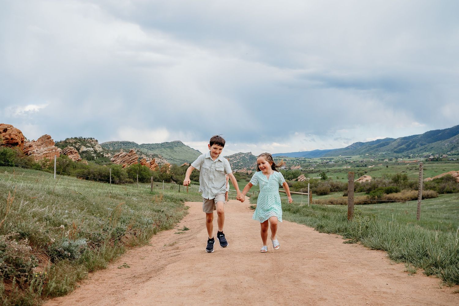 Brother and sister playfully running down dirt path at South Valley Park, stunning red rocks views in background.