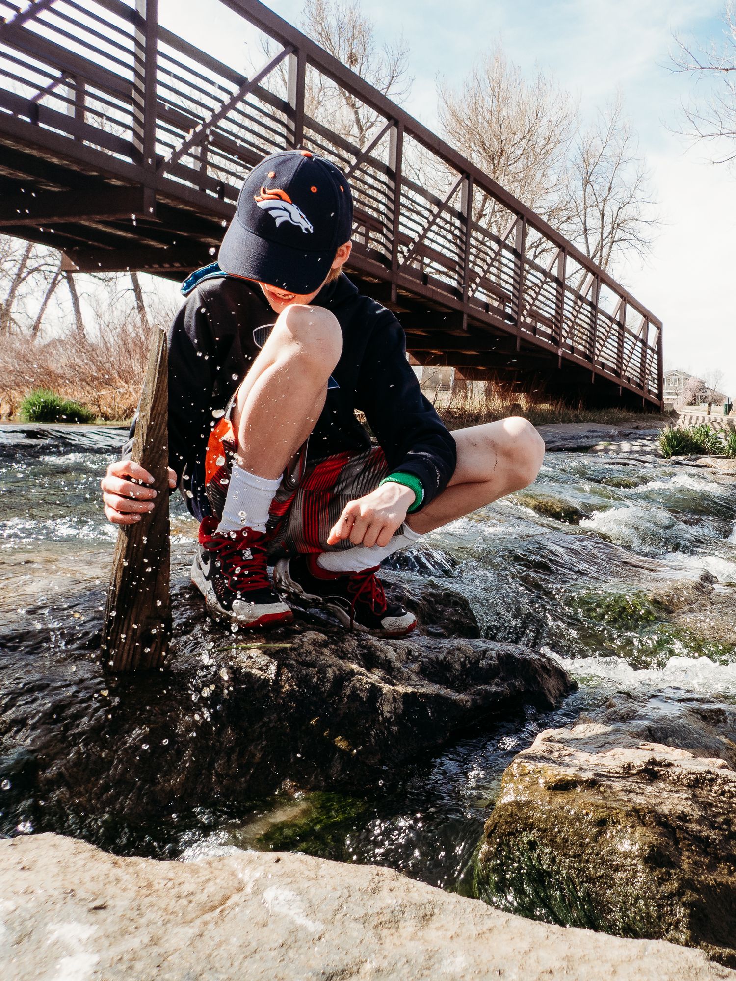 Tween boy playing in river, bridge in background.