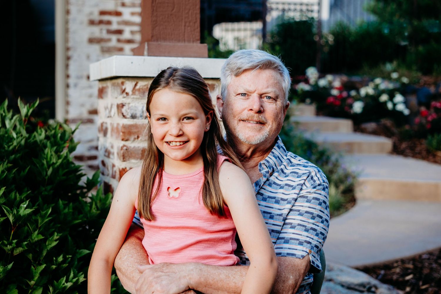 Young girl sitting on grandfather's lap in beautiful Centennial, CO backyard.