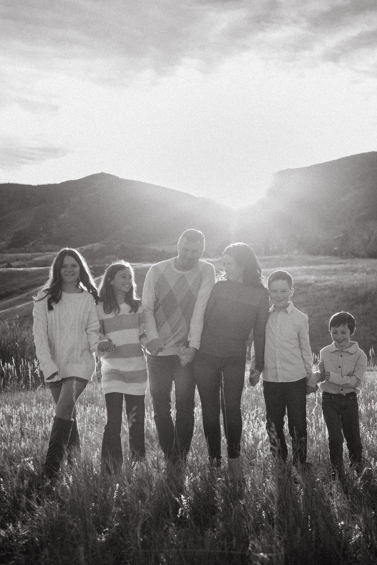 Black and white portrait of blended family walking in foothills with sunburst in backgroun.