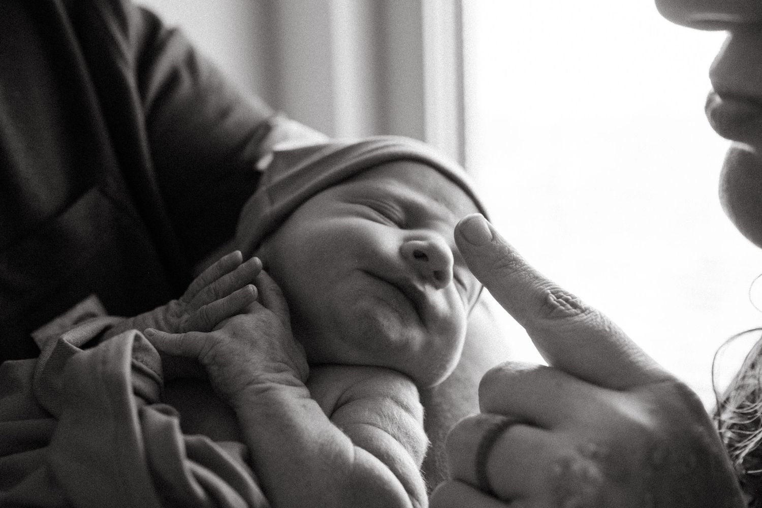 Black and white close up of father holding baby and mother reaching out to touch newborn's tiny nose.