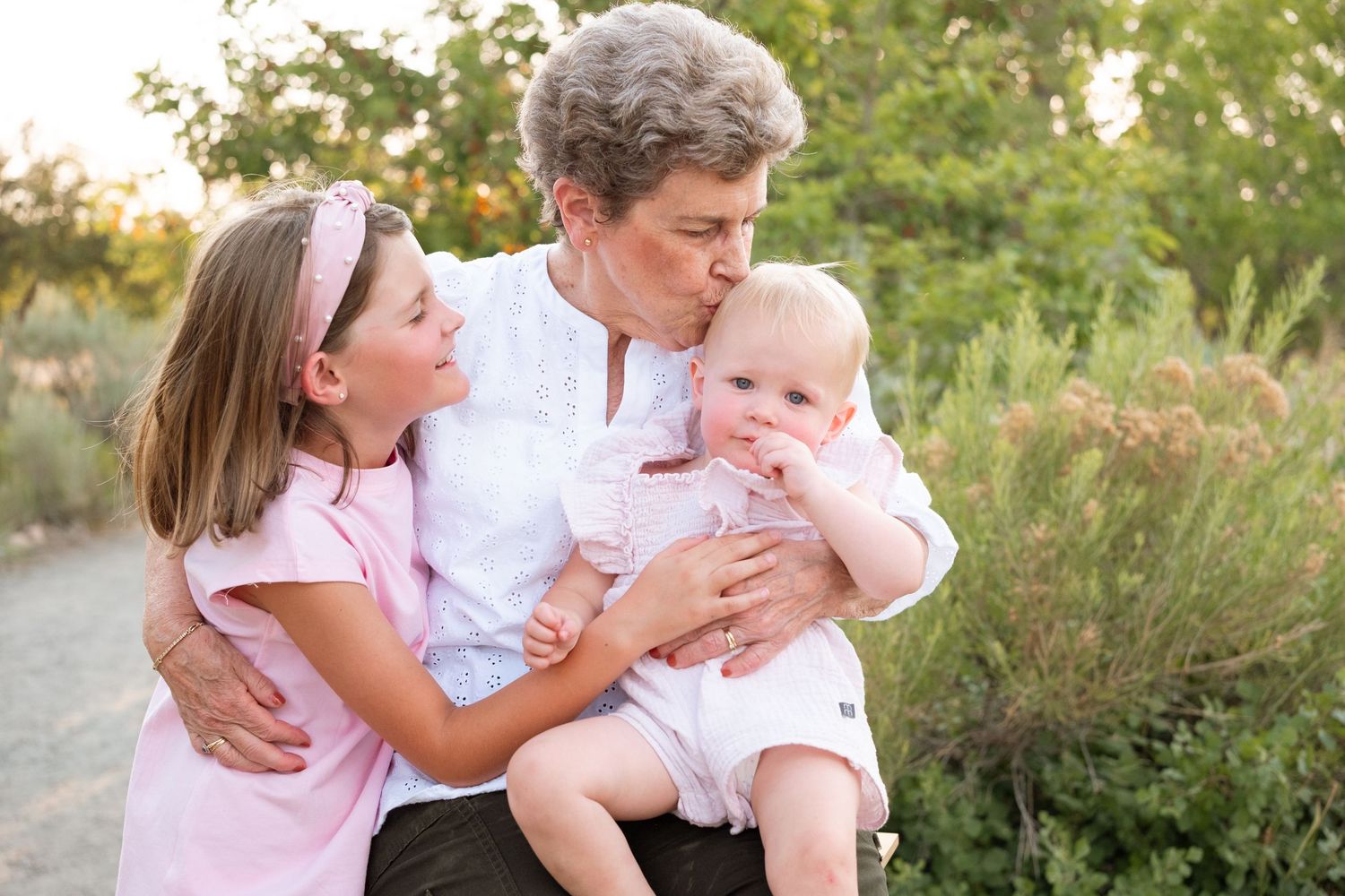 Grandmother holding granddaughter on her lap while snuggling other granddaughter on her other side.