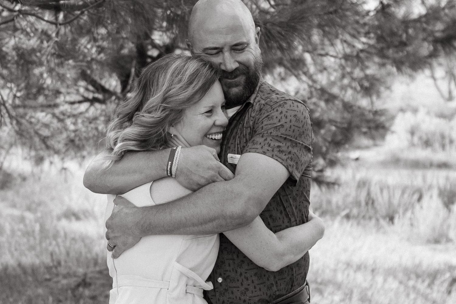 Black and white portrait of adult couple embracing, both smiling with eyes closed.