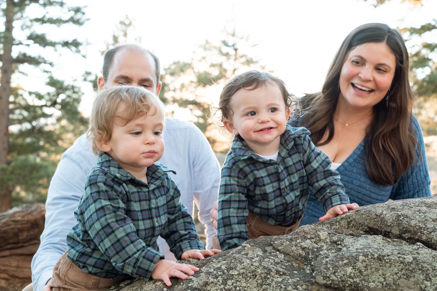 Mother, father and twin one year olds playing on large boulder, all smiling.