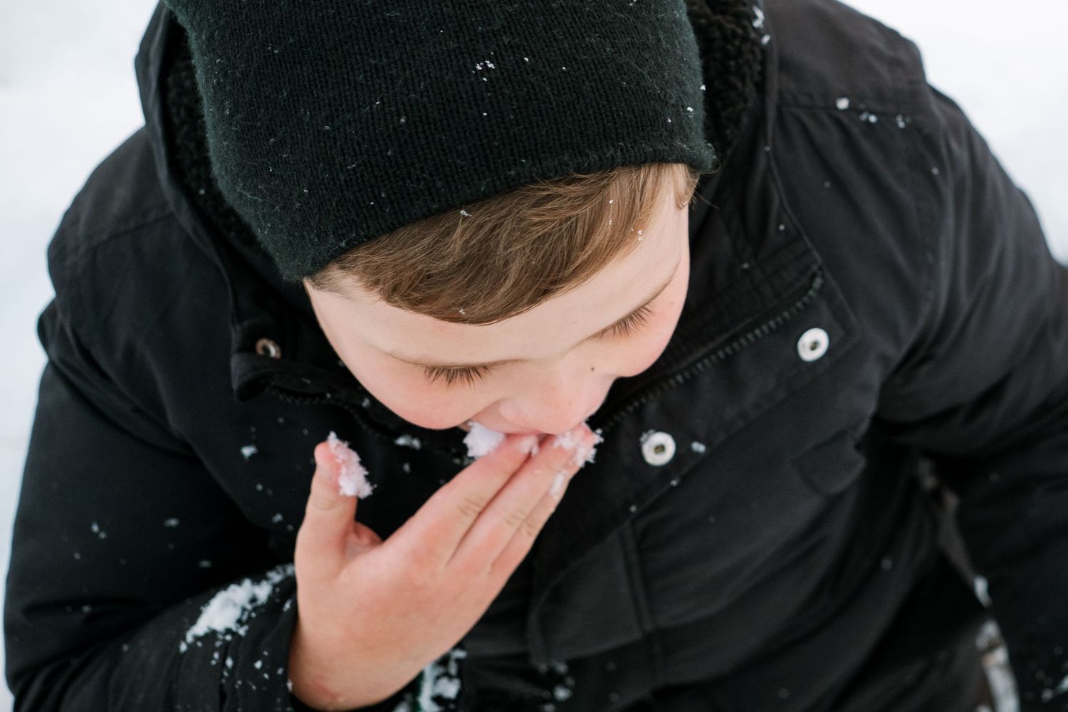 Young boy with autism eating snow flakes off finger tips.
