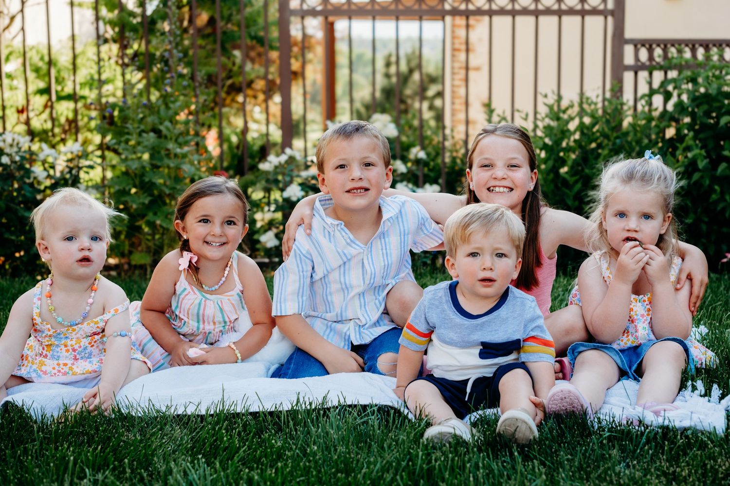 Six cousins of various ages sitting on blanket in beautiful Centennial backyard.