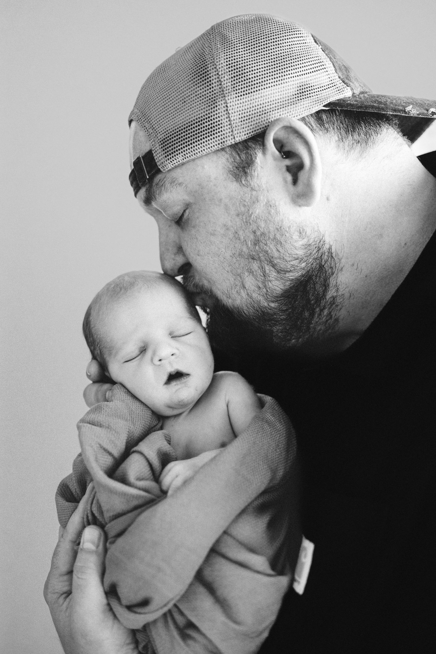 Black and white portrait of dad kissing baby's temple in Fresh 48 session.