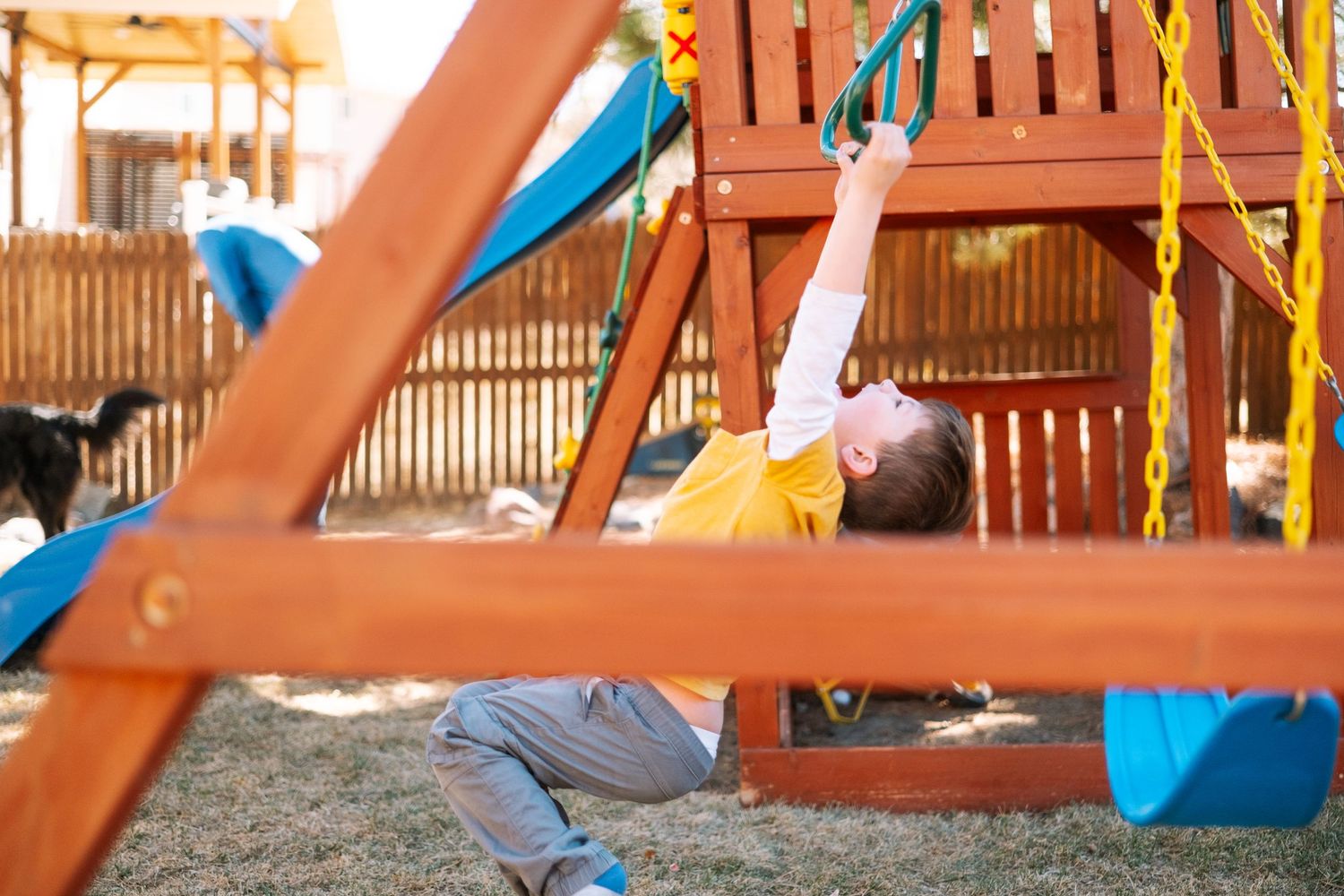 Young boy playing on climbing equipment in backyard playground.