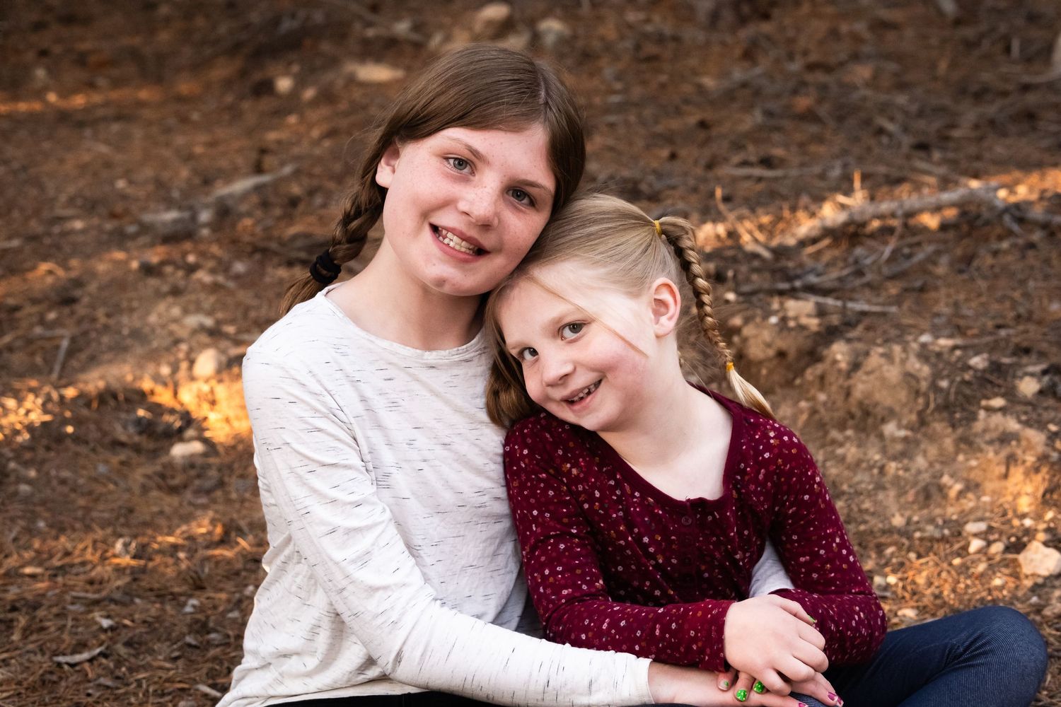 Two young sisters sitting closely together, smiling.