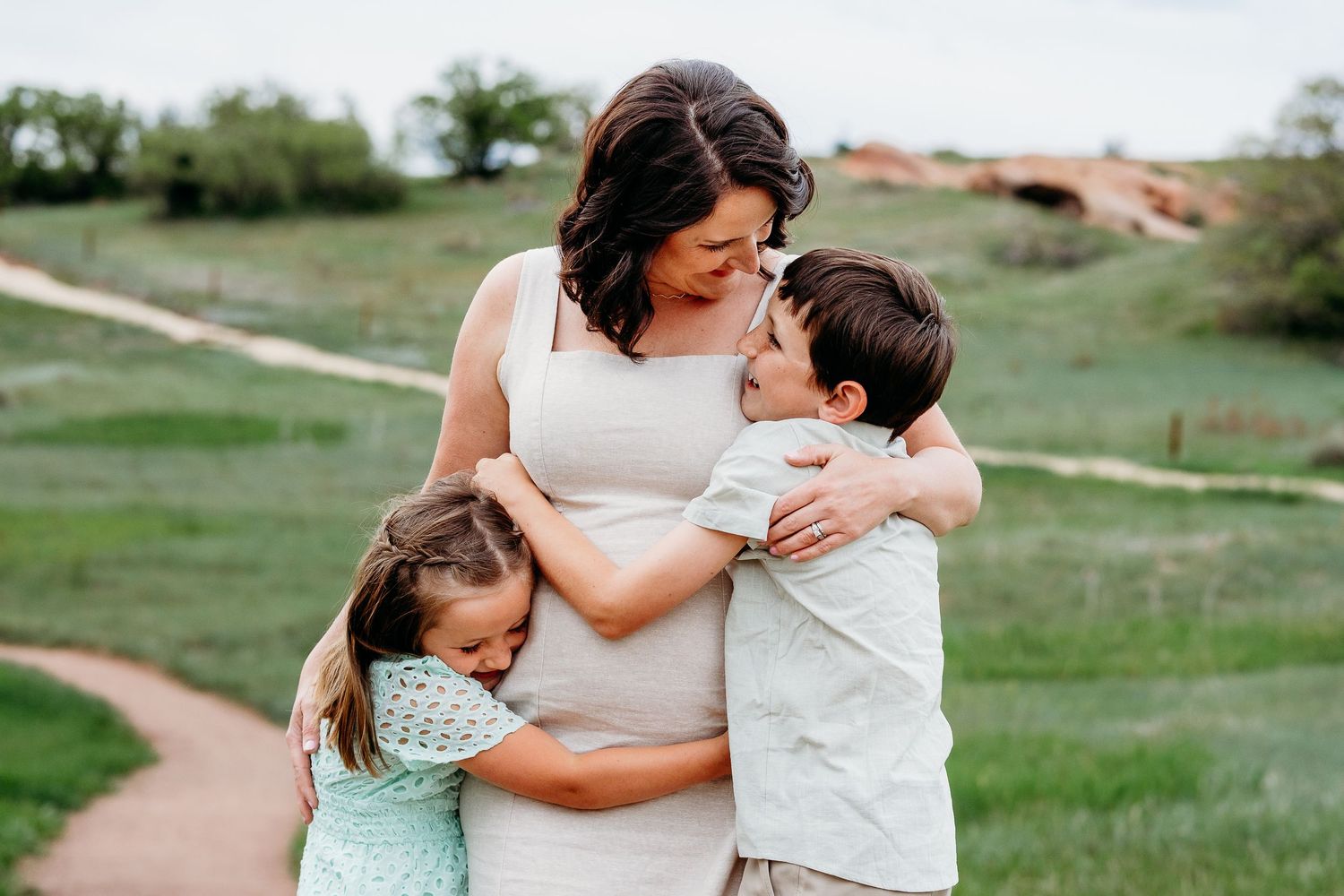 Mother standing in middle, daughter and son hugging her from each side, all three smiling as they hug tightly