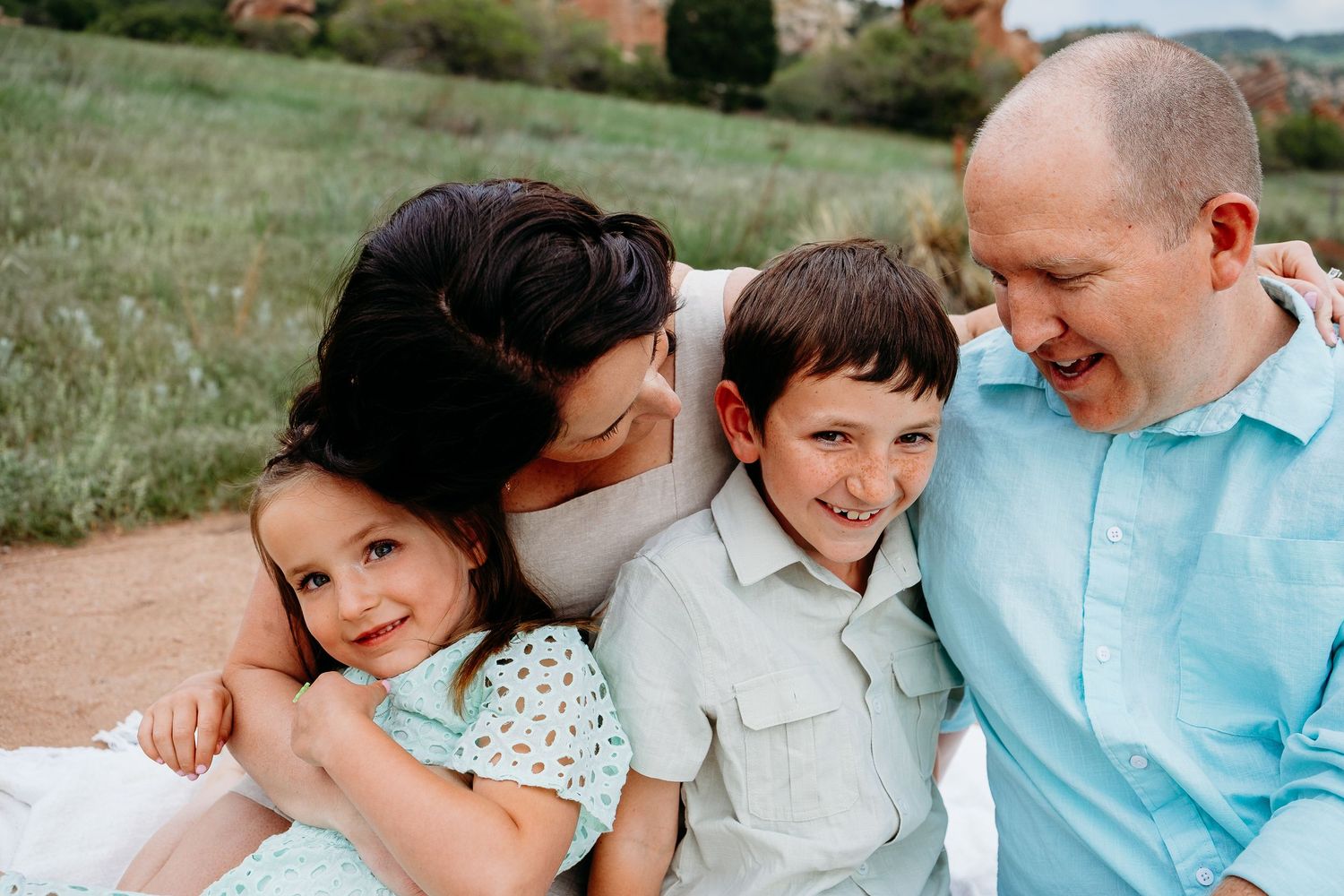 Family of four snuggled closely, mom and dad smiling at kids.