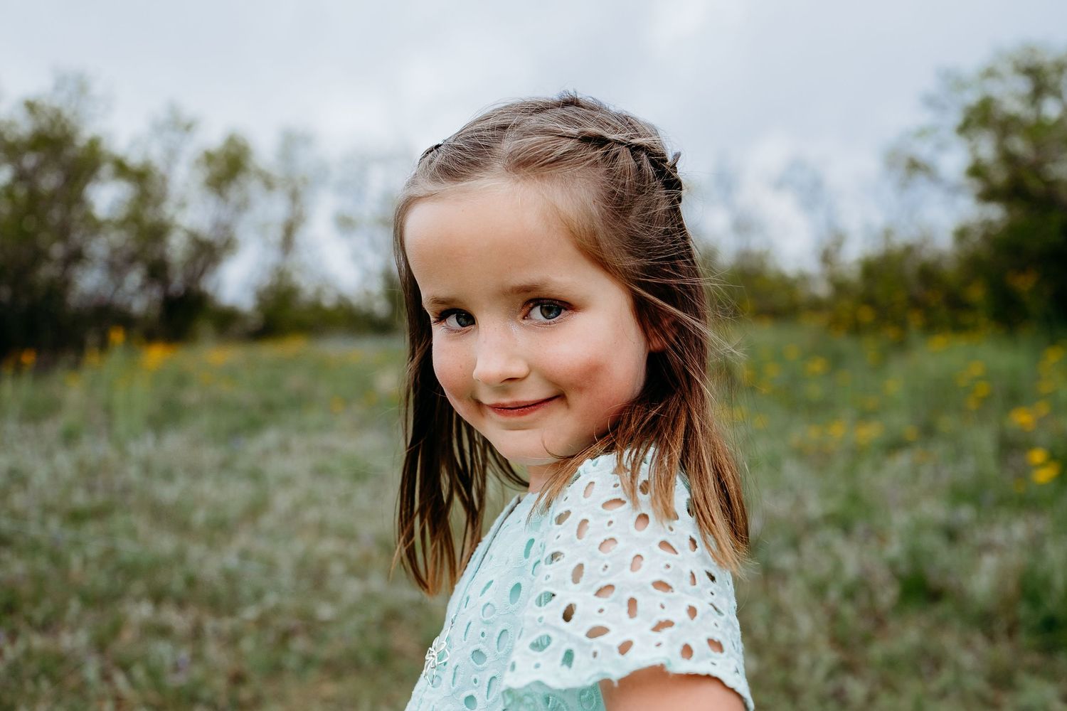 Portrait of young girl smiling, greenery and flowers in background.