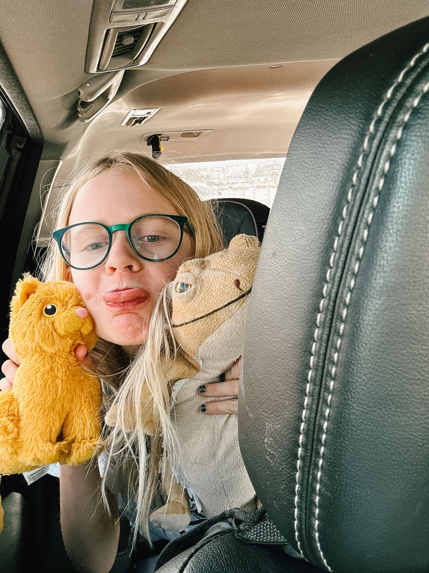 Denver photographer's project 365, June, close up of young girl holding two stuffed animals, sticking out her tongue.