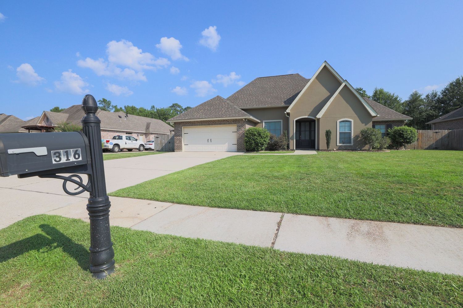 Modern suburban house with beige exterior, attached garage and well-maintained front lawn with mailbox.
