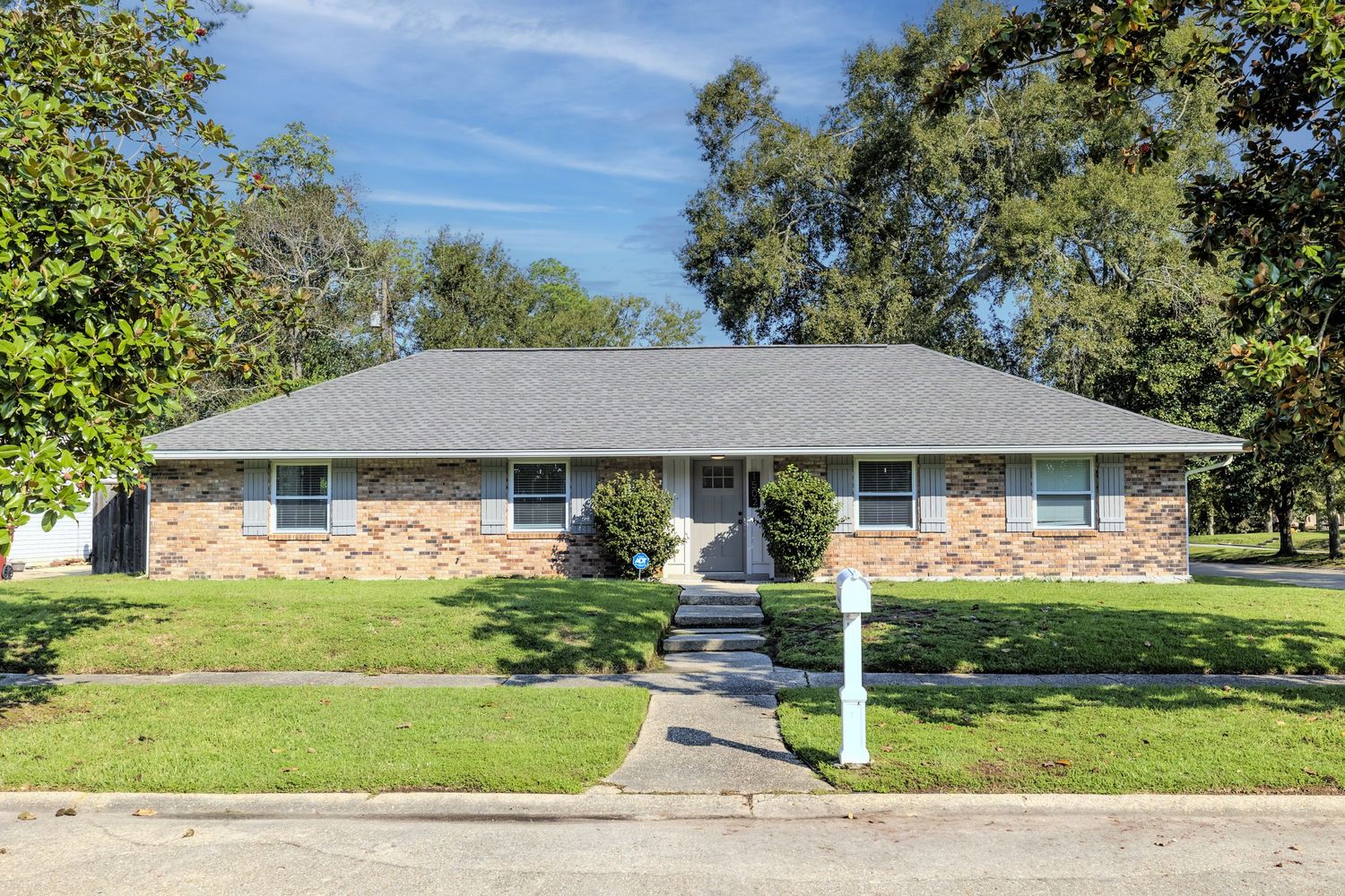 Single story ranch home with brick and stone exterior, grey roof, and paved pathway leading to front door.