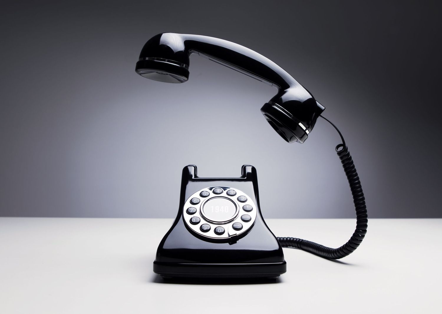 A black vintage rotary telephone with lifted handset photographed against a dark background.