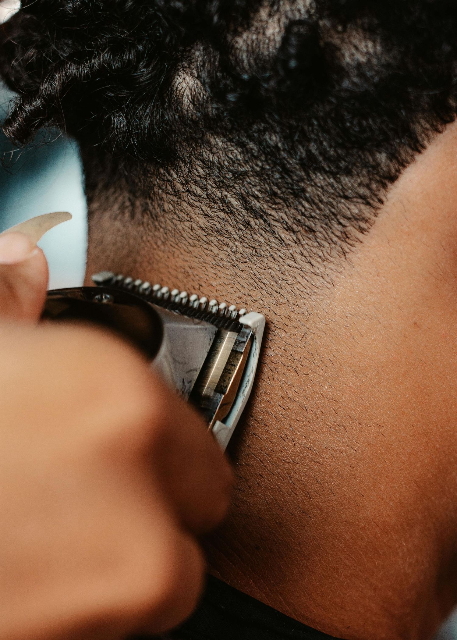 Close-up shot of a barber using electric clippers to trim and fade hair at the neckline.