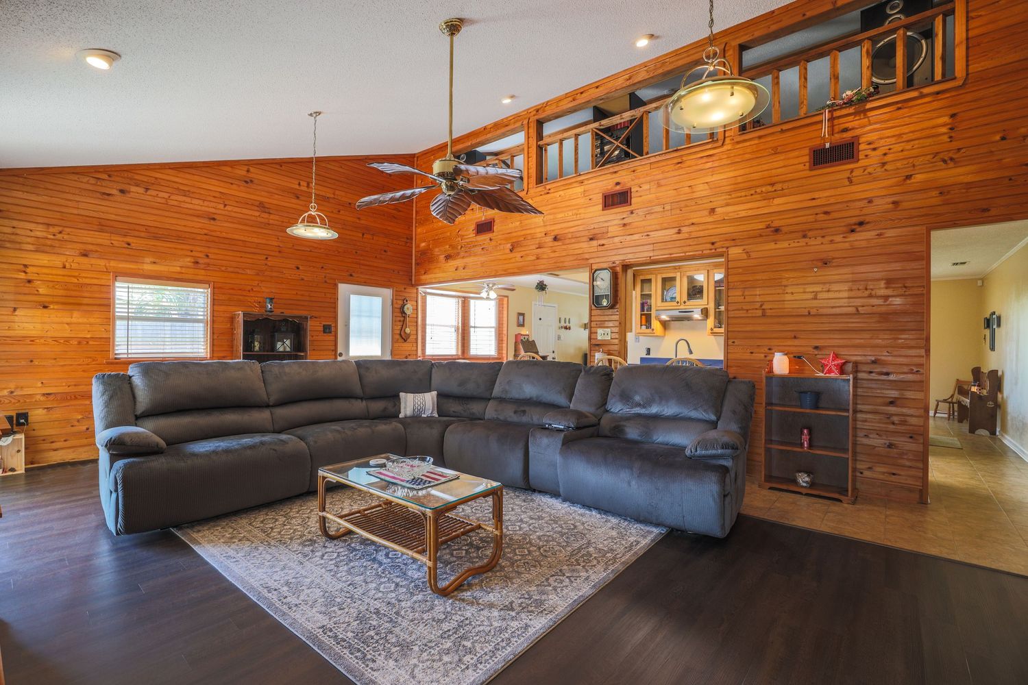 Rustic living room with wood paneled walls, grey sectional sofa, and hardwood floors in a cozy cabin-style interior.
