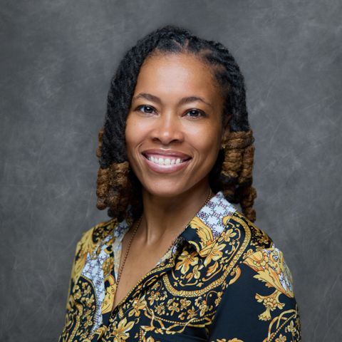 Professional studio portrait showing a bright smile and ombre two-toned braided hairstyle, wearing a patterned blue and gold blouse.