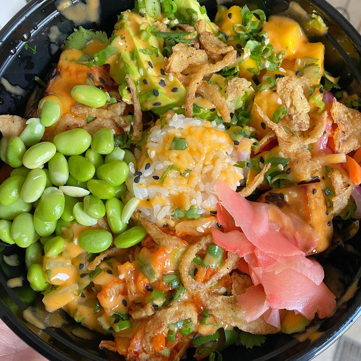 Colorful poke bowl with fresh fish, edamame beans, ginger, salad greens and mango garnished with sesame seeds.