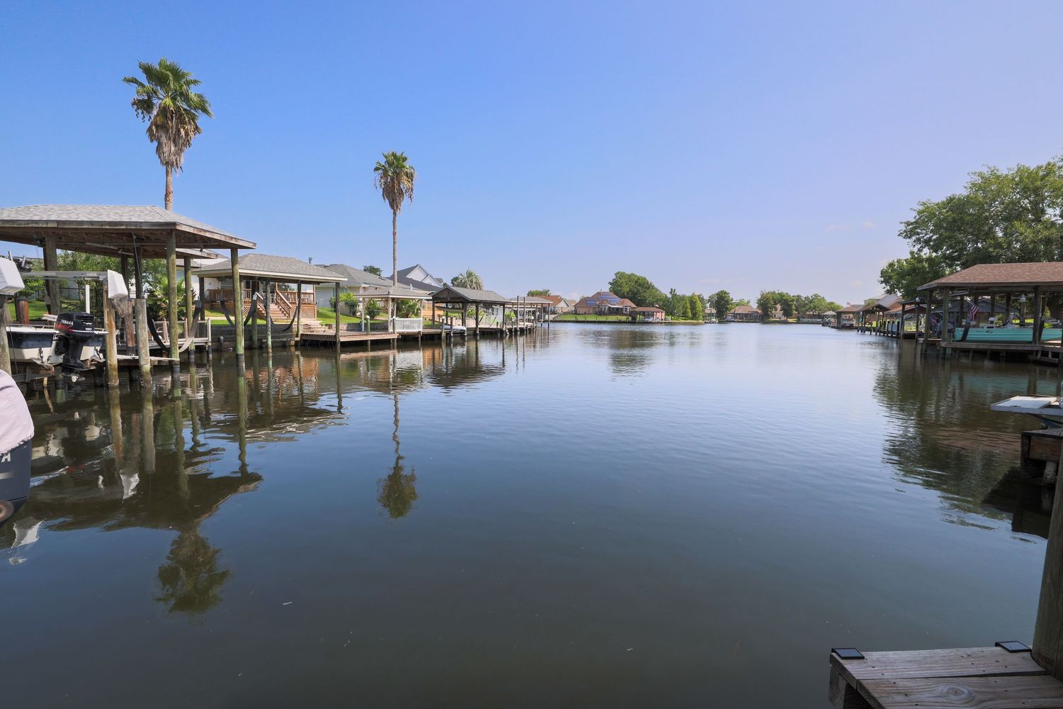 Panoramic view of waterfront homes and palm trees along a calm canal with boats docked at private piers.