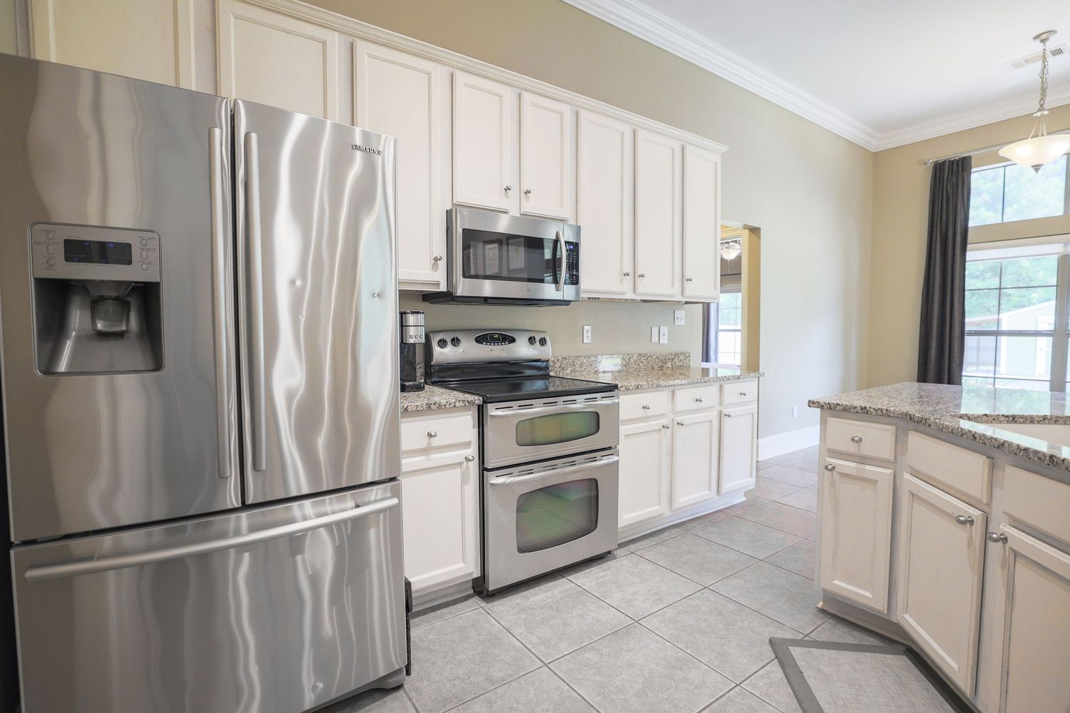 Modern white kitchen featuring light cream cabinets, stainless steel appliances, and a curved counter layout with tiled floors.