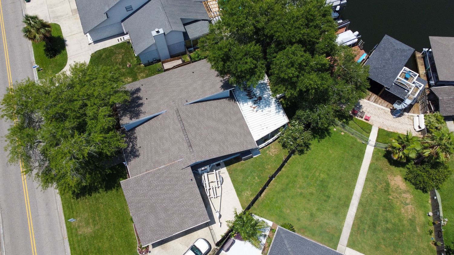 Aerial view of a residential home with gray shingle roof surrounded by mature trees and a driveway.