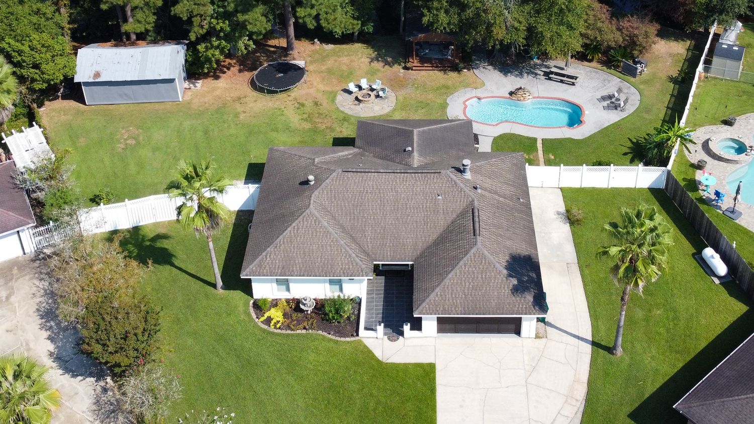 Aerial drone view of a modern single-story home with swimming pool and palm trees in a sunny residential neighborhood.