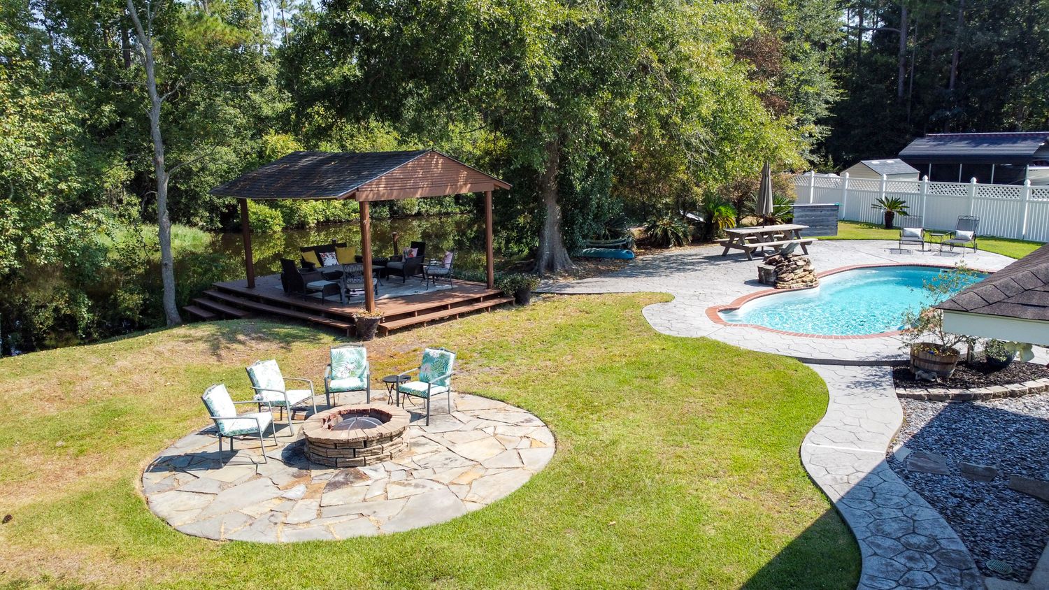 Aerial view of a backyard oasis featuring a swimming pool, covered gazebo, and circular patio with lounge chairs.