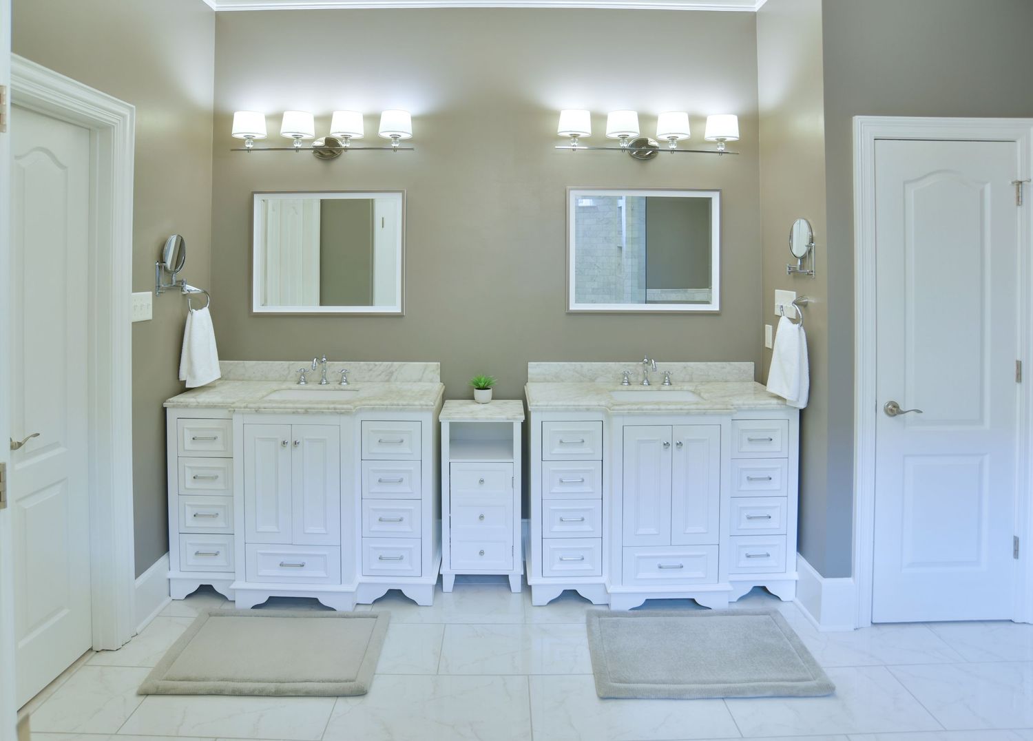 Modern white bathroom vanity with double sinks, sconce lighting, and white cabinets in a neutral beige interior.