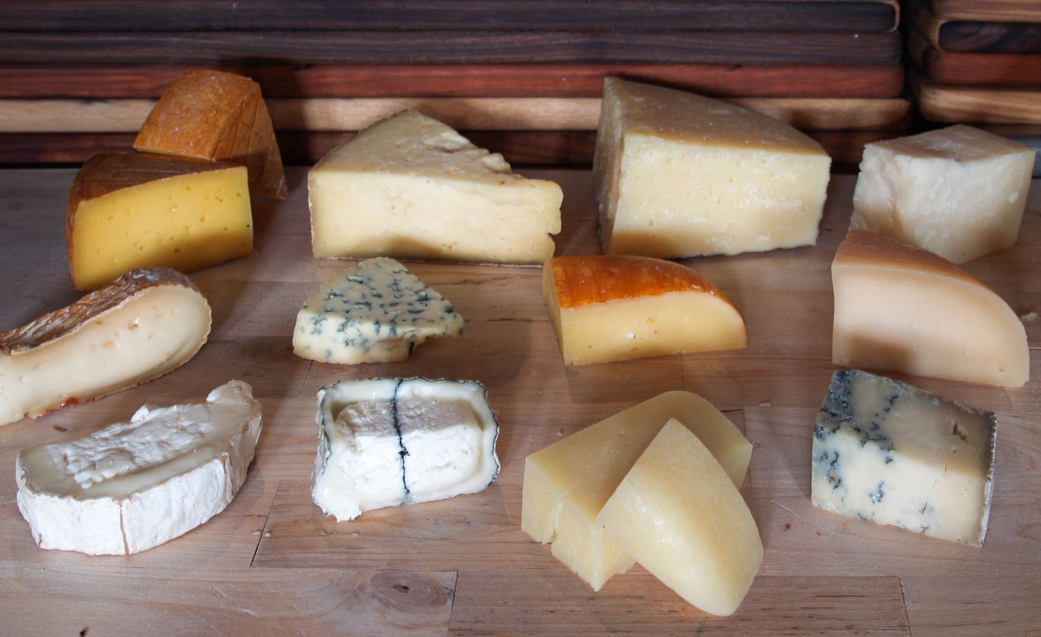 Various chunks of artisanal cheeses including blue cheese and aged hard cheeses arranged on a wooden cutting board.