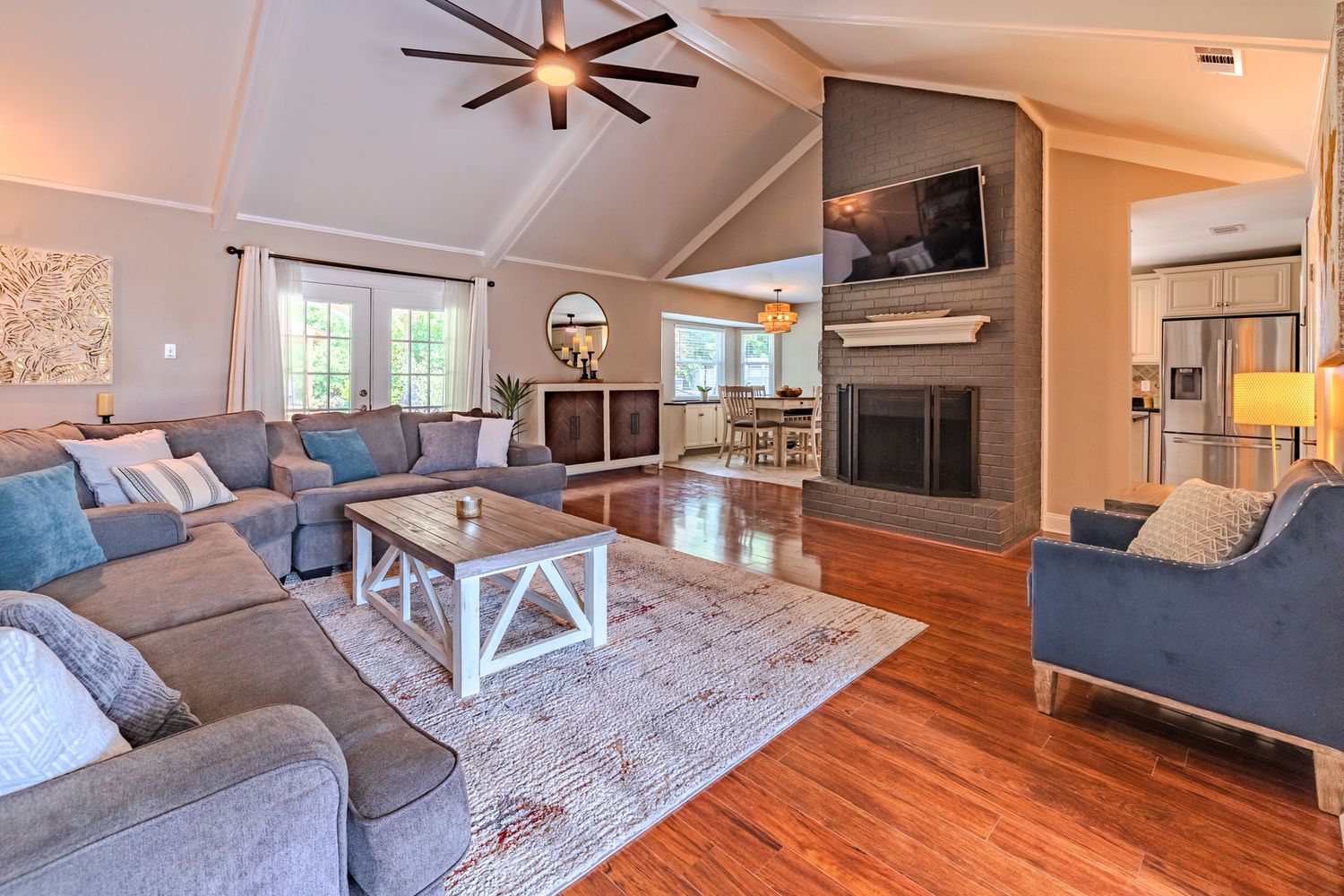 Modern open concept living room features hardwood floors, gray sofa, and large windows letting in natural light.