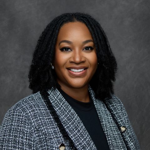 Professional headshot of person in tweed blazer and black top with natural curly hair style against grey backdrop.