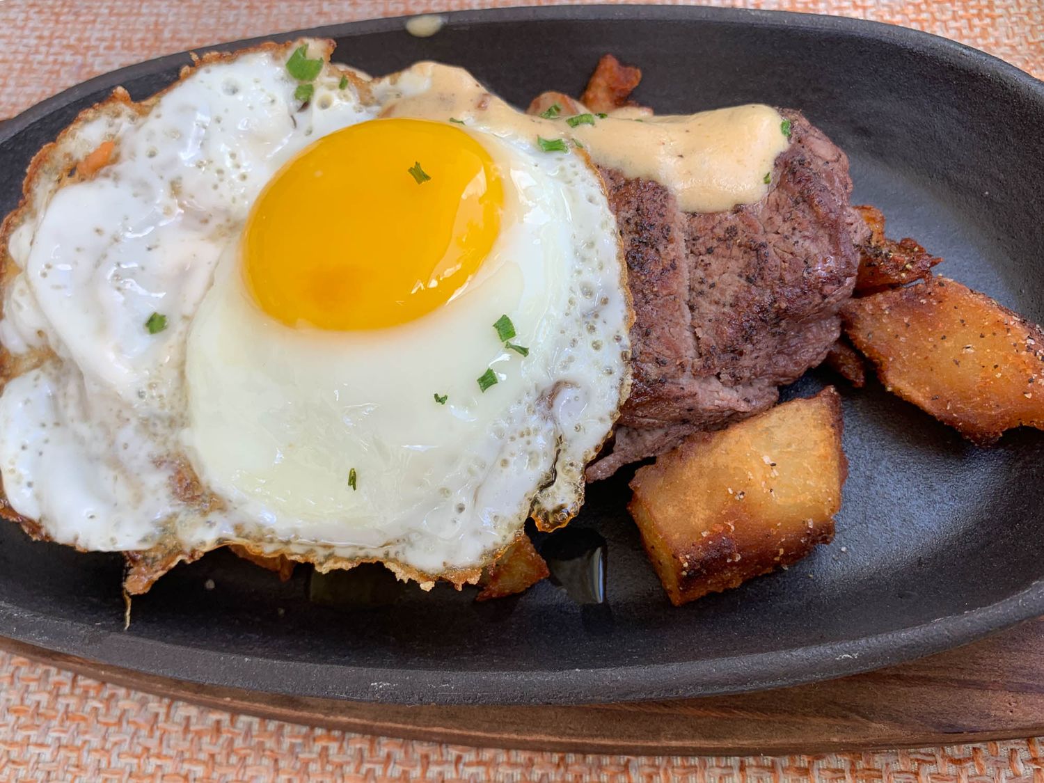 Sunny side up egg served with seared beef and roasted potatoes on a sizzling cast iron plate.