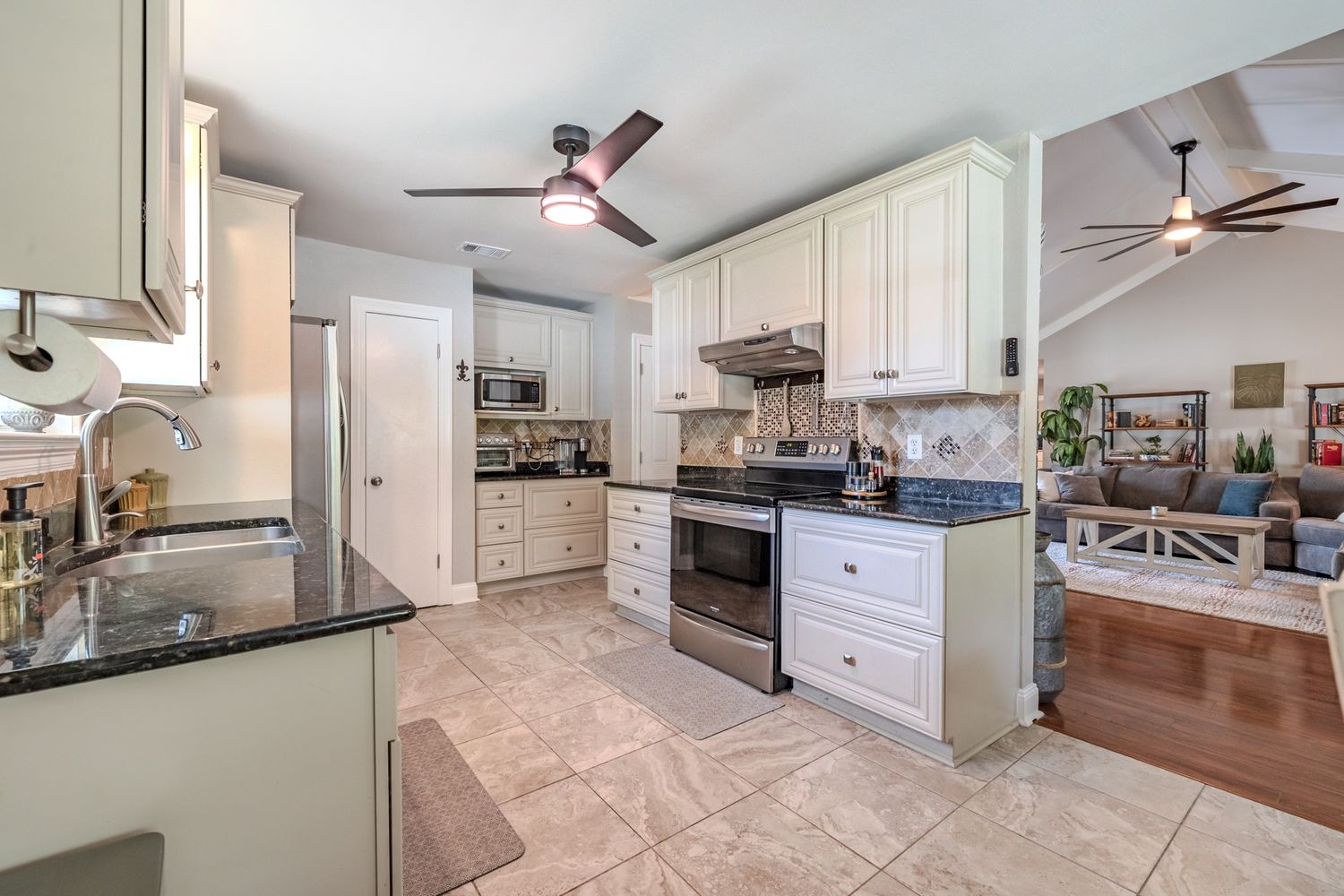 Modern white kitchen with ceiling fans features stainless steel appliances and granite countertops in an open layout design.