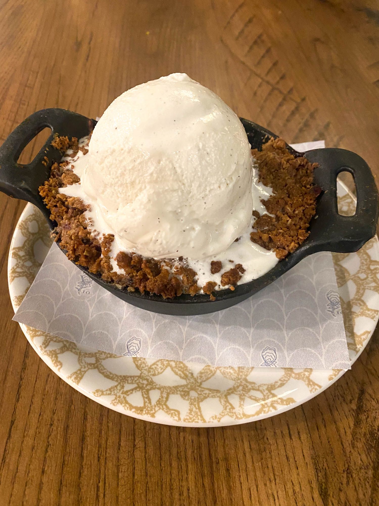 A scoop of vanilla ice cream nestled in a cast iron skillet with crumbled cookie crust on a decorative plate.