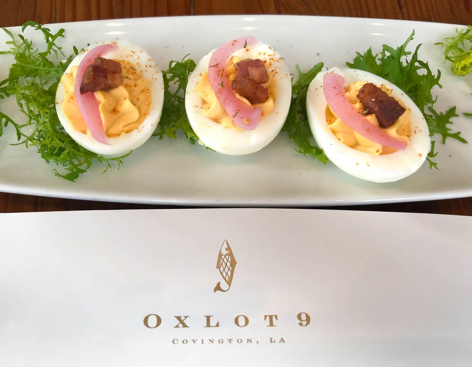 Gourmet deviled eggs topped with prosciutto and garnished with fresh greens on a white plate at Oxlot 9 restaurant.