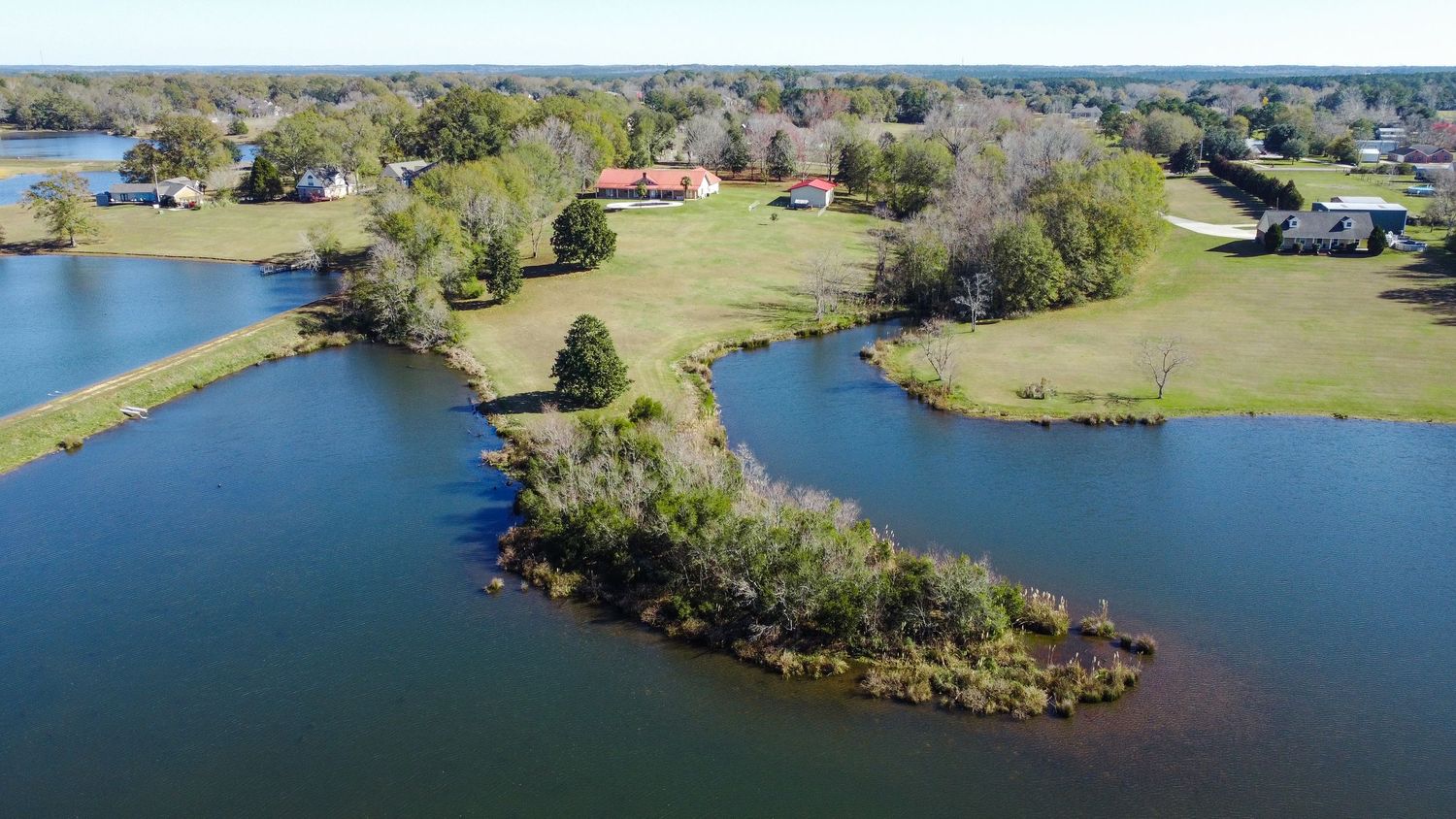 Aerial view of a scenic peninsula with green landscaping surrounded by bright blue lake waters on a sunny day.