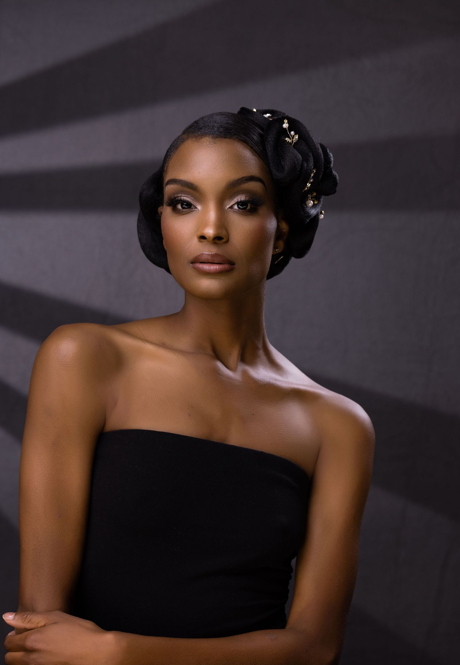 Elegant portrait against gray backdrop features strapless black dress and intricate updo hairstyle with delicate accessories.