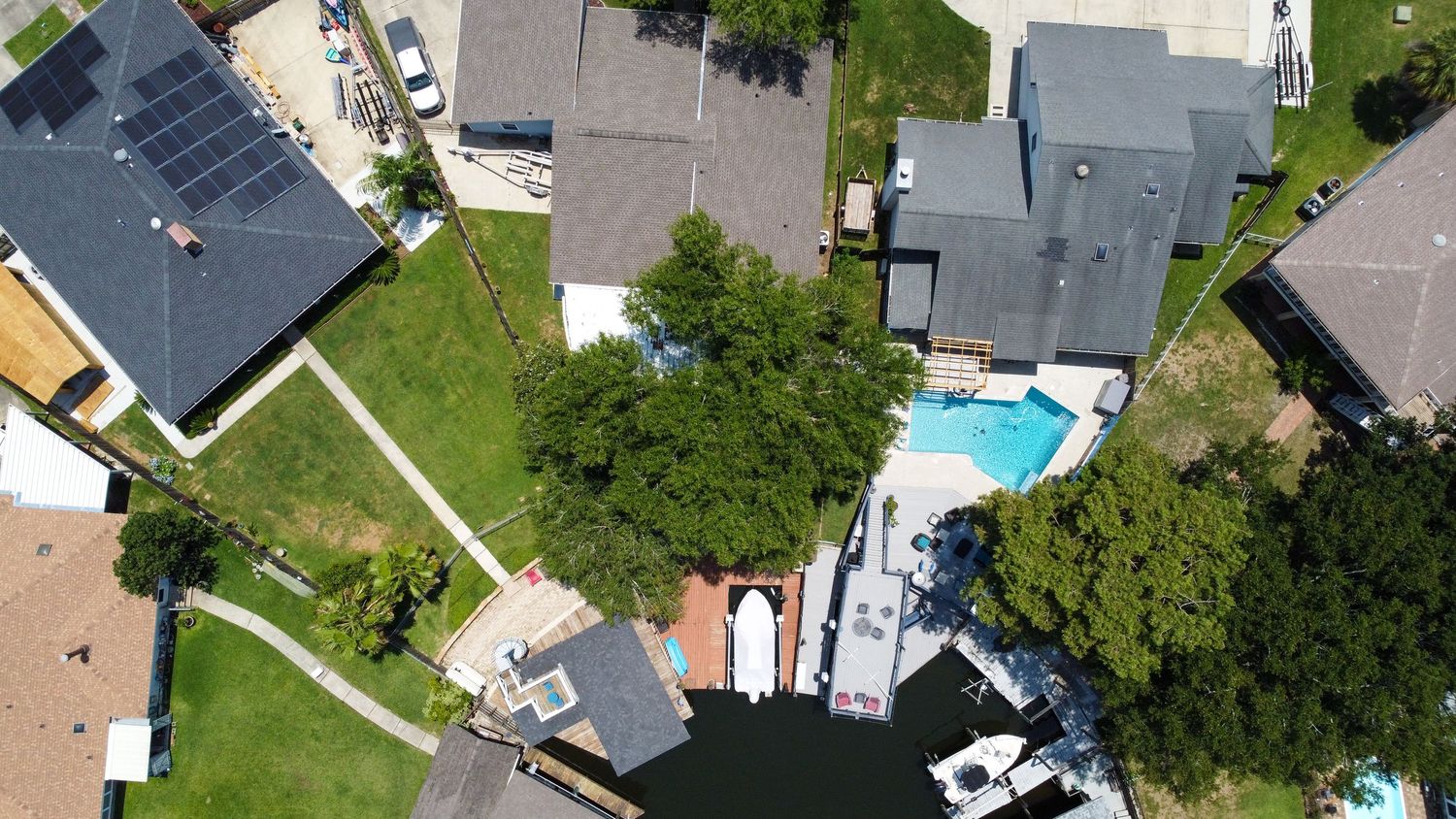 Aerial drone view of residential homes with swimming pools and well-manicured lawns on a sunny day.