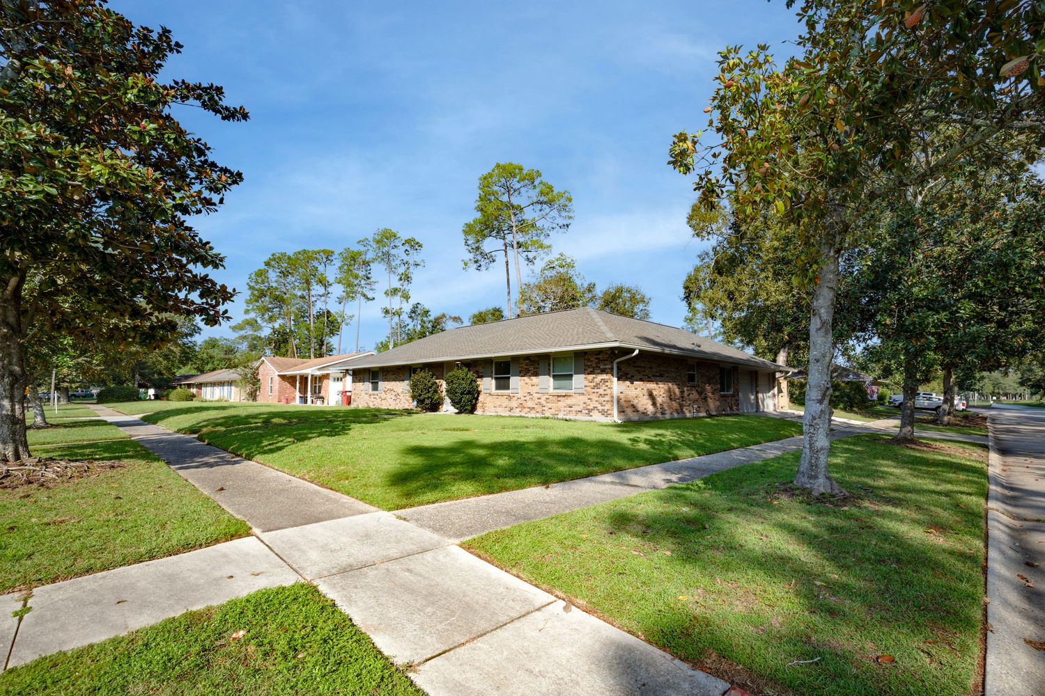 Mid-century modern ranch style home with low-pitched roof and landscaped yard viewed from street corner on sunny day.