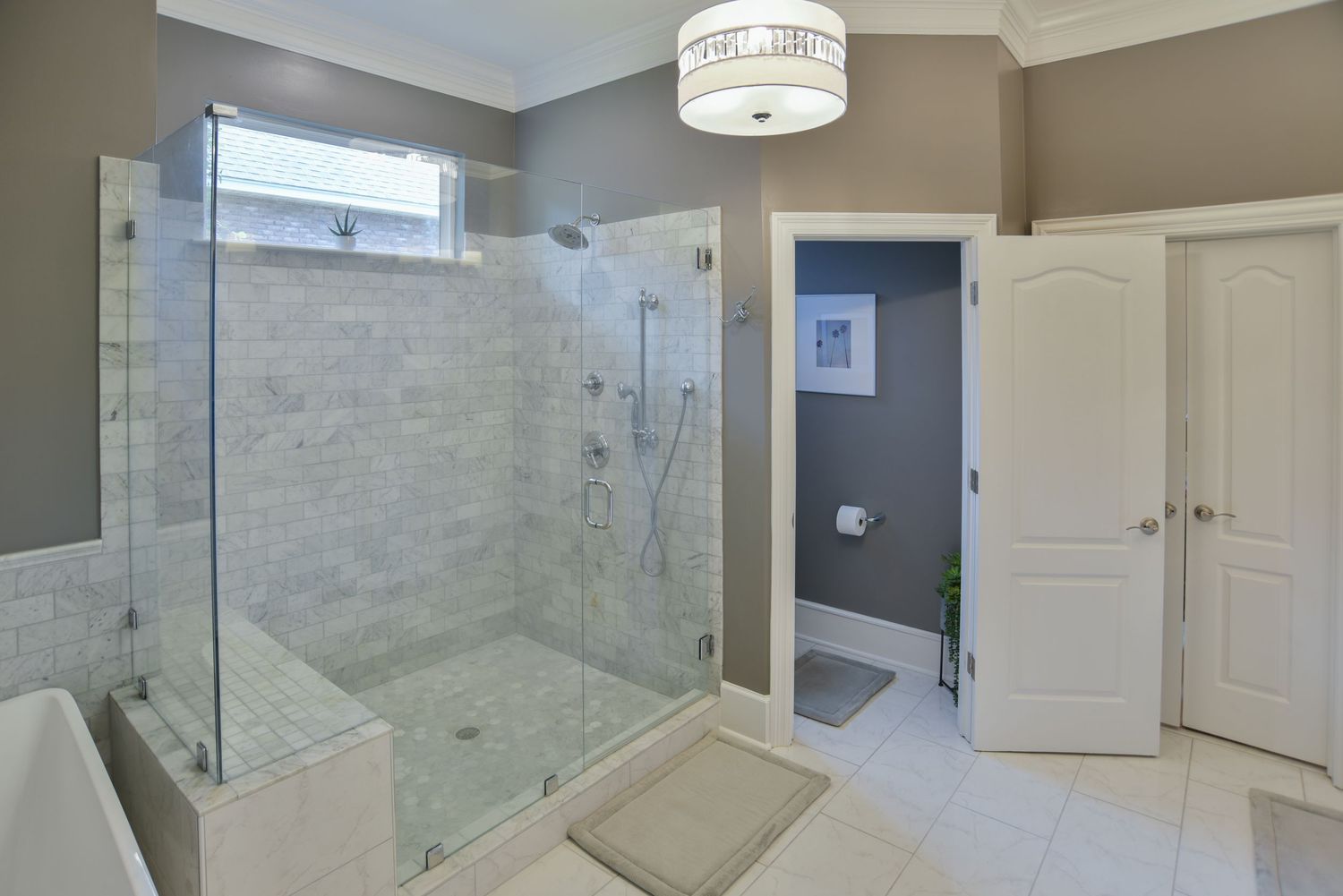 Modern bathroom with glass shower enclosure, marble tile walls, and drum light fixture.