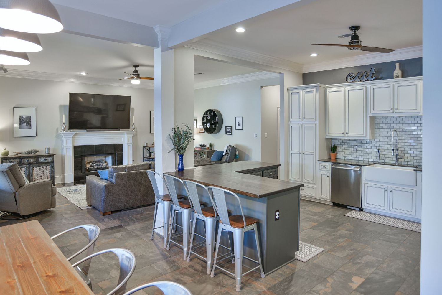 Modern open concept living space with white kitchen, gray island, metal bar stools and adjacent family room with fireplace.