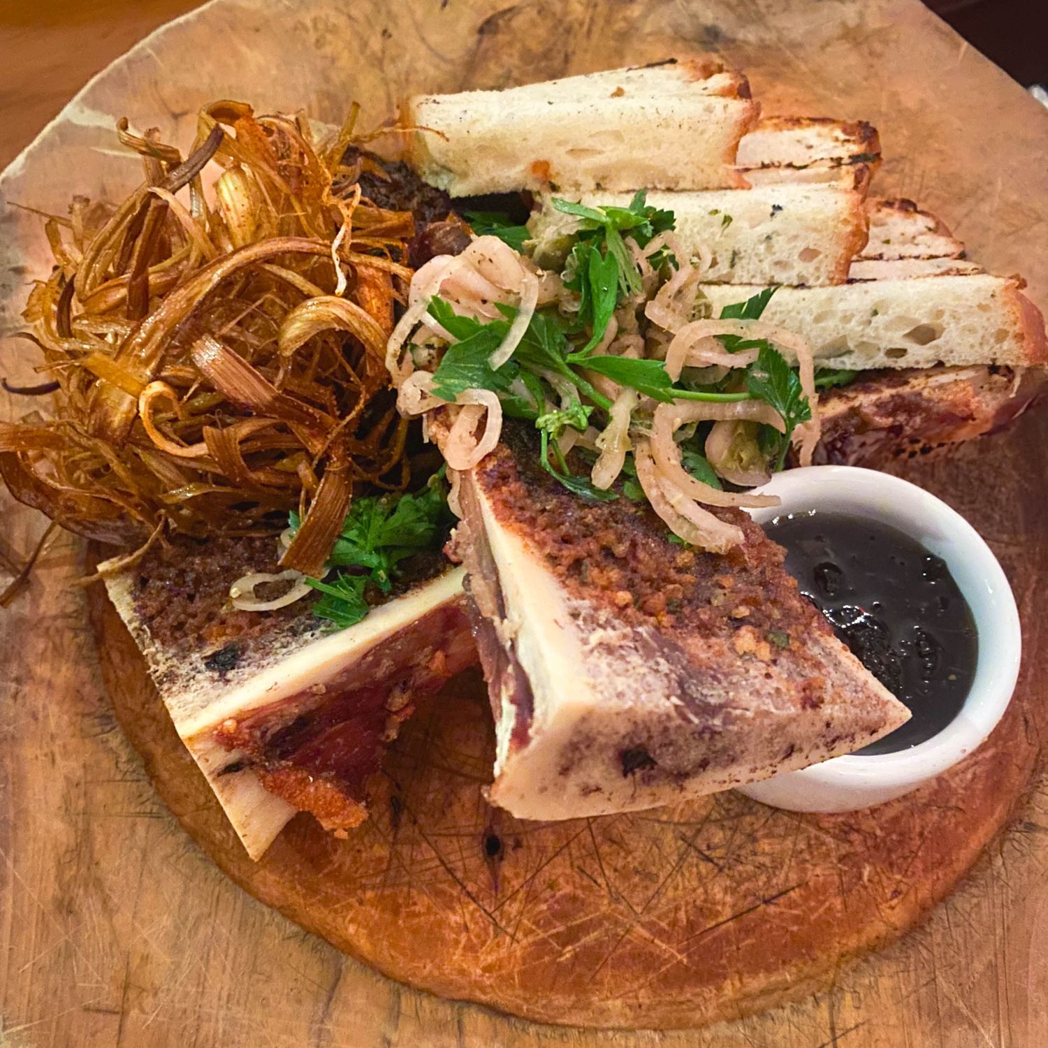 Grilled sandwich with crispy onion strings and au jus dipping sauce served on rustic wooden board.